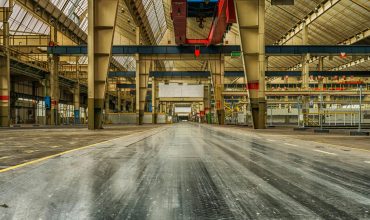 Wide view of an empty industrial warehouse with visible cranes and metal structures.